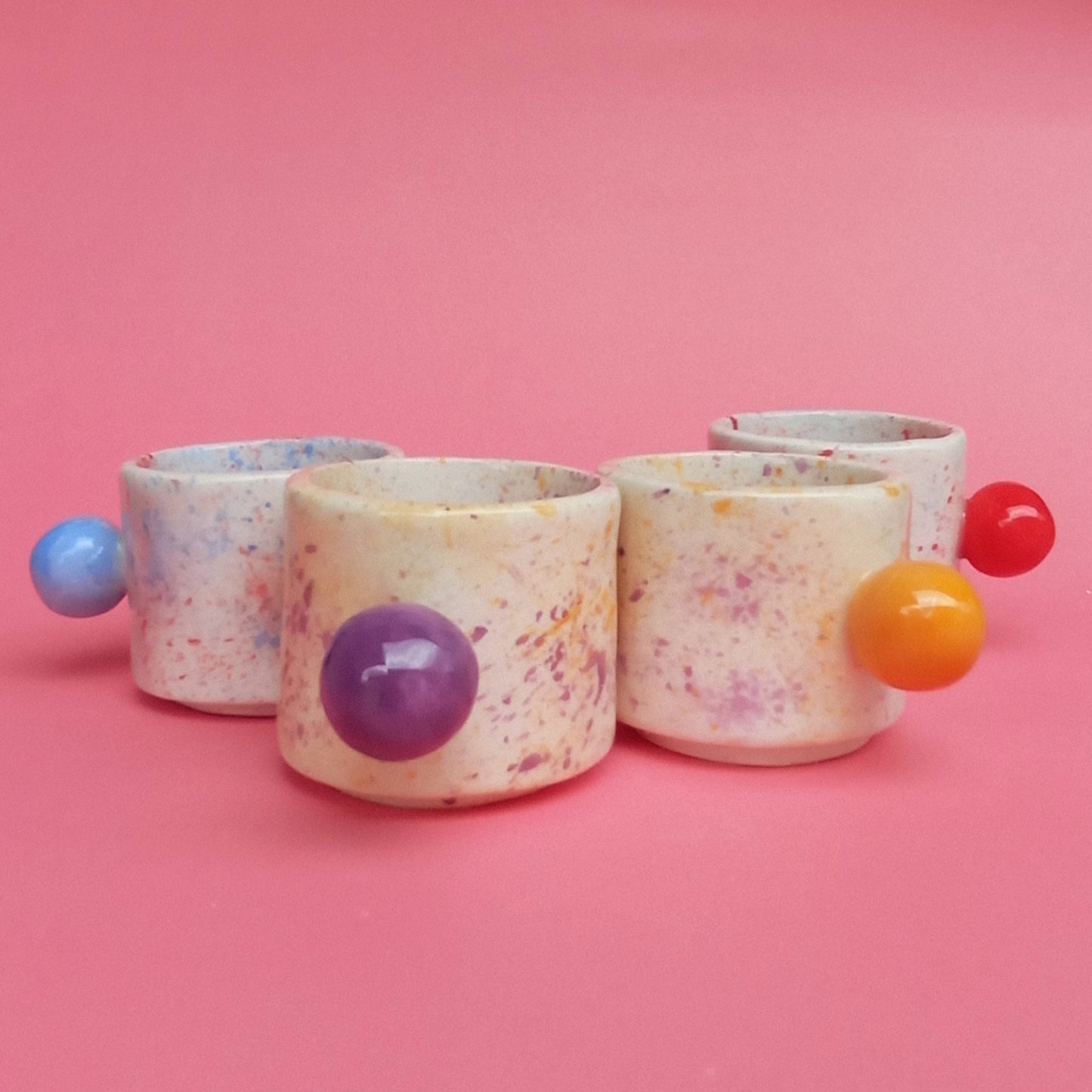 Set of colorful ceramic containers with spherical handles on a pink background