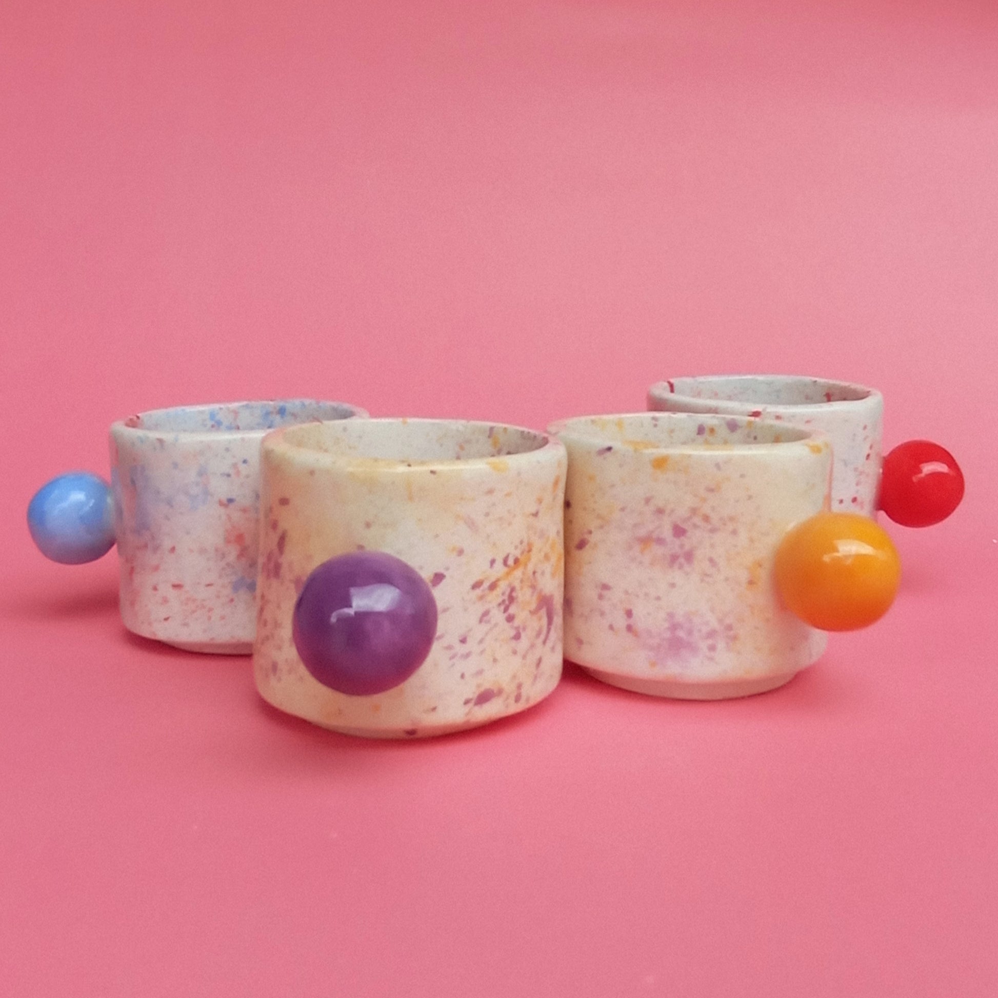 Set of colorful ceramic containers with spherical handles on a pink background