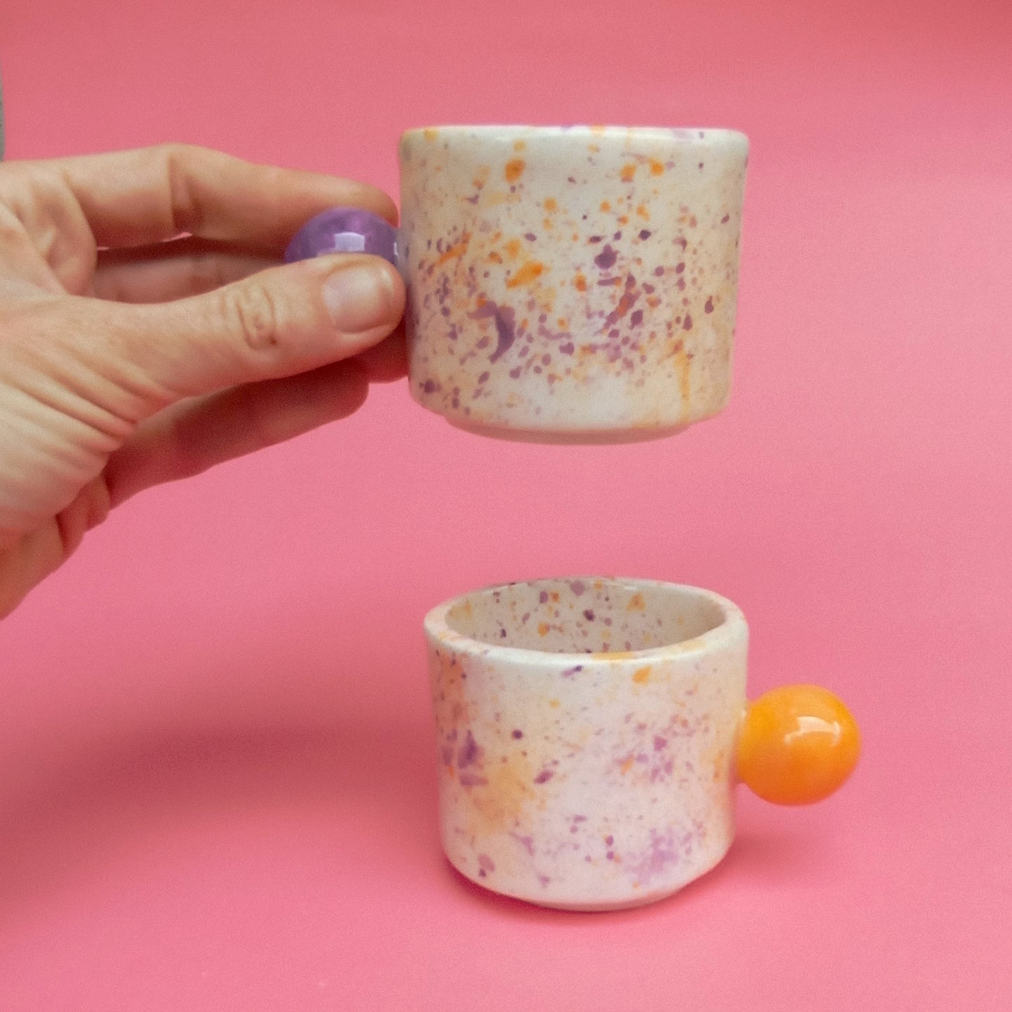 Speckled ceramic cup held by a hand with a pink background