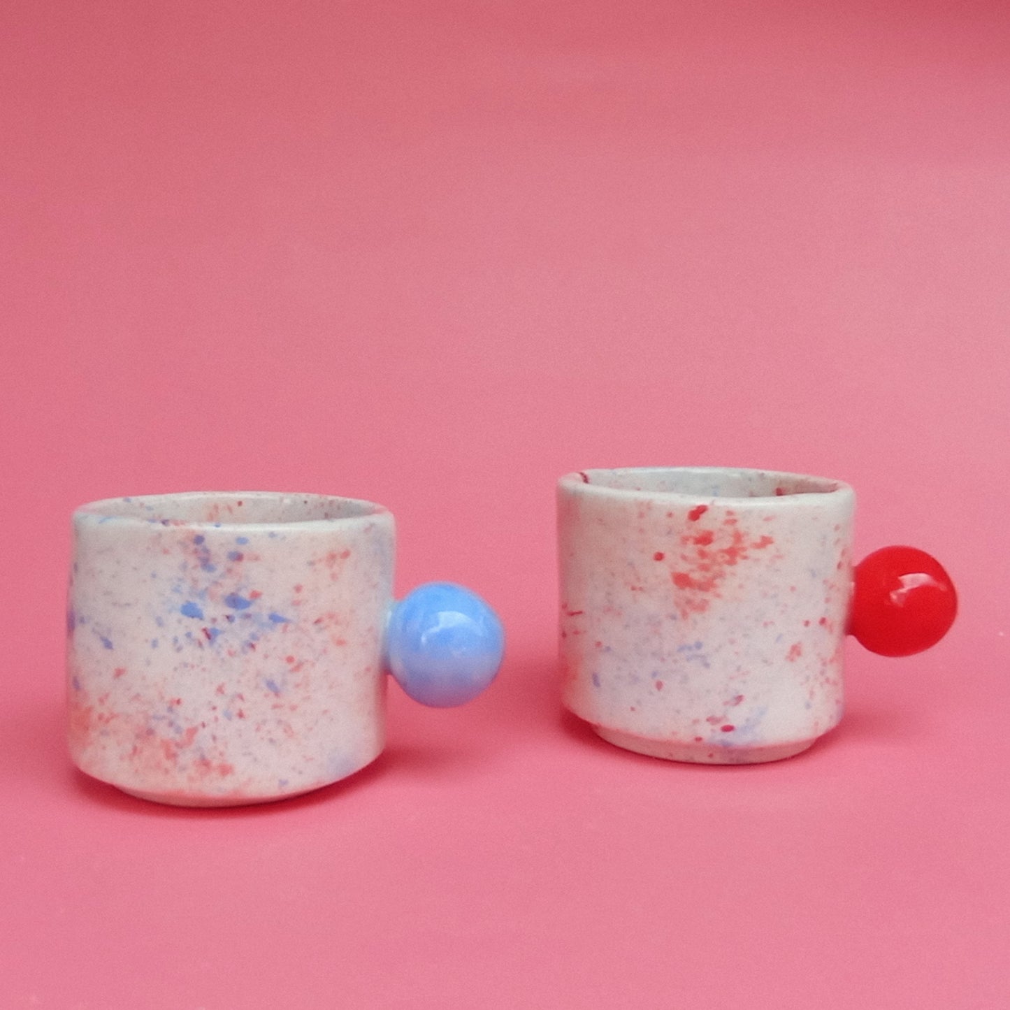 Two speckled ceramic cups with colorful balls on a pink background