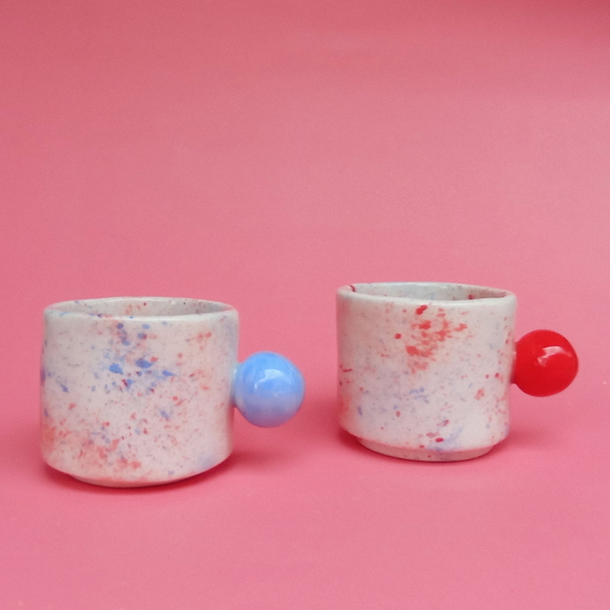 Two speckled ceramic cups with colorful balls on a pink background