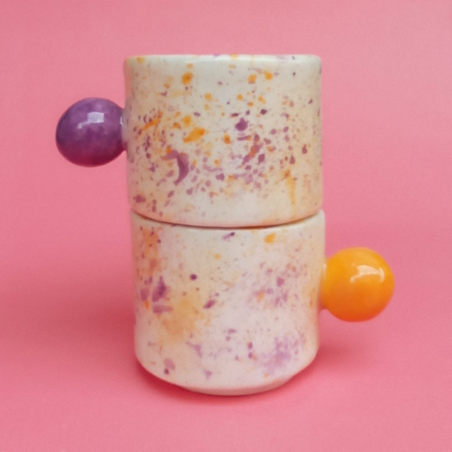 Speckled ceramic container with purple and orange handles on a pink background